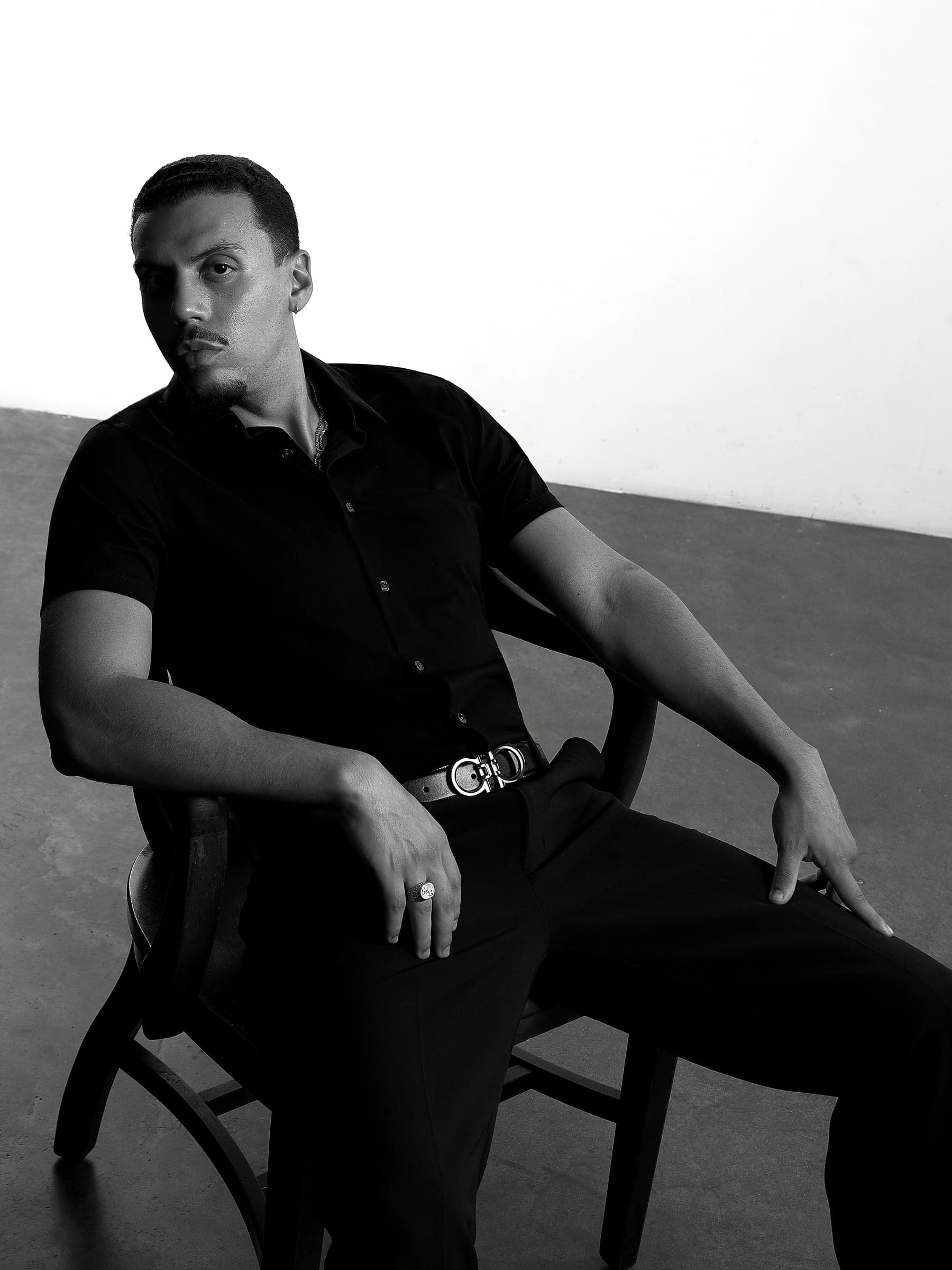 Mars seated in a black shirt, one arm resting on the chair, looking straight into the camera